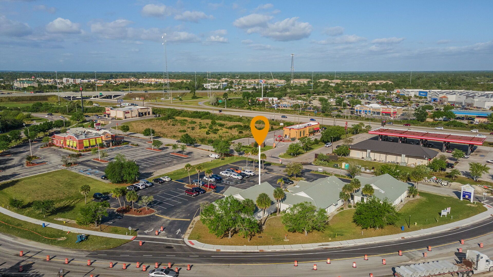 Aerial view of a shopping plaza with parking lots, stores, and a large location marker pin.