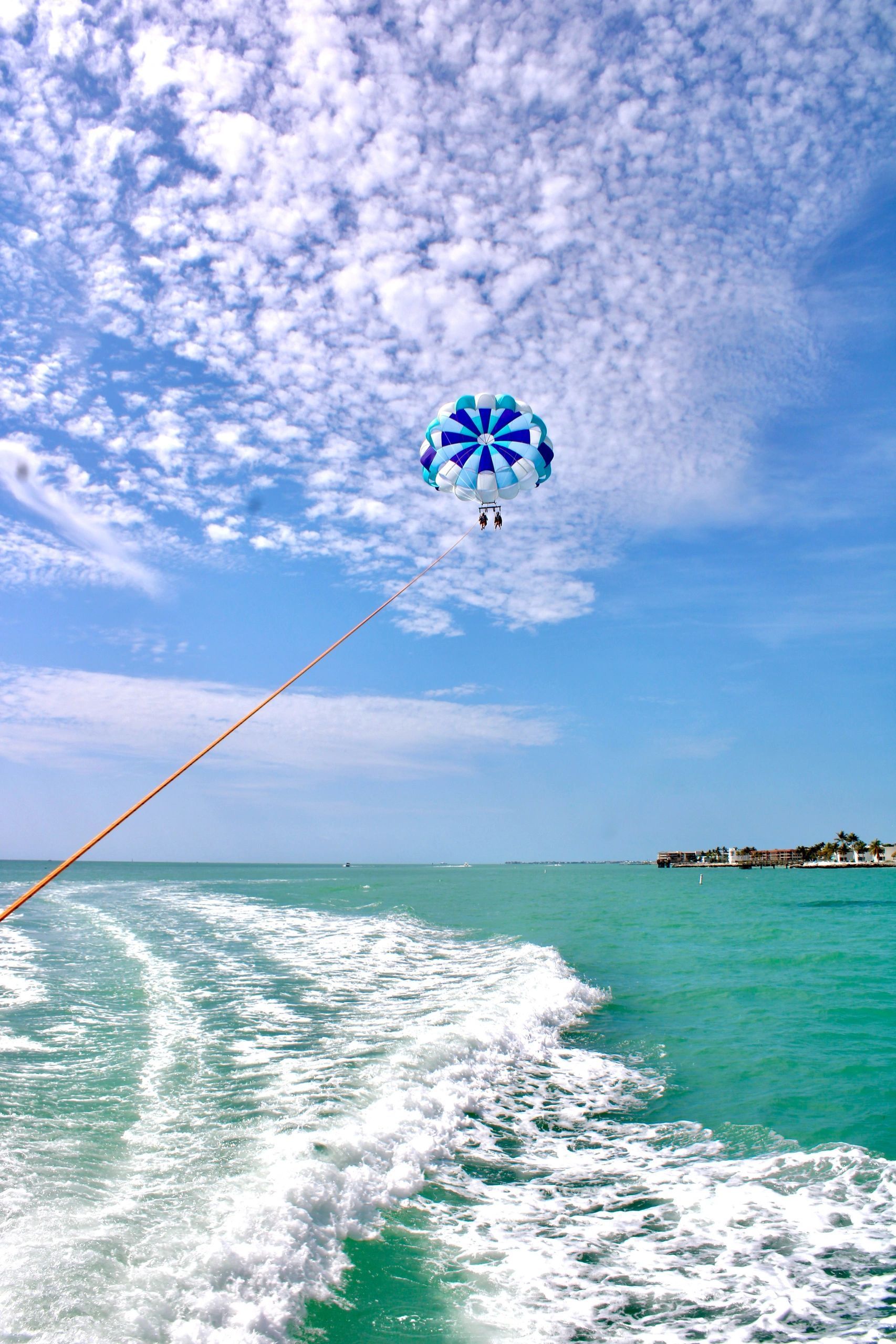 A person is parasailing over the ocean from a boat.