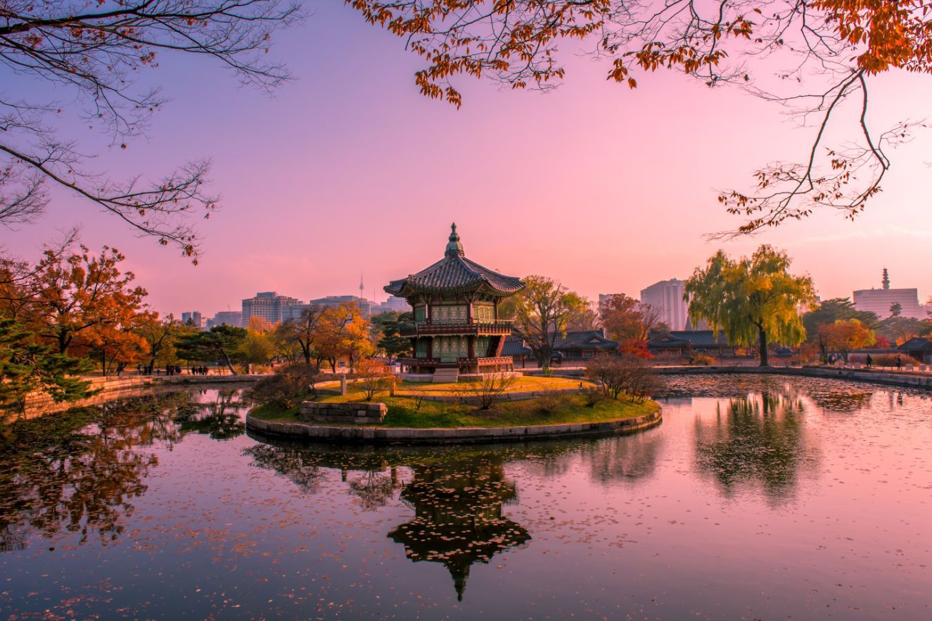 A serene view of a traditional Korean pavilion in a pond, autumn foliage, sunset.