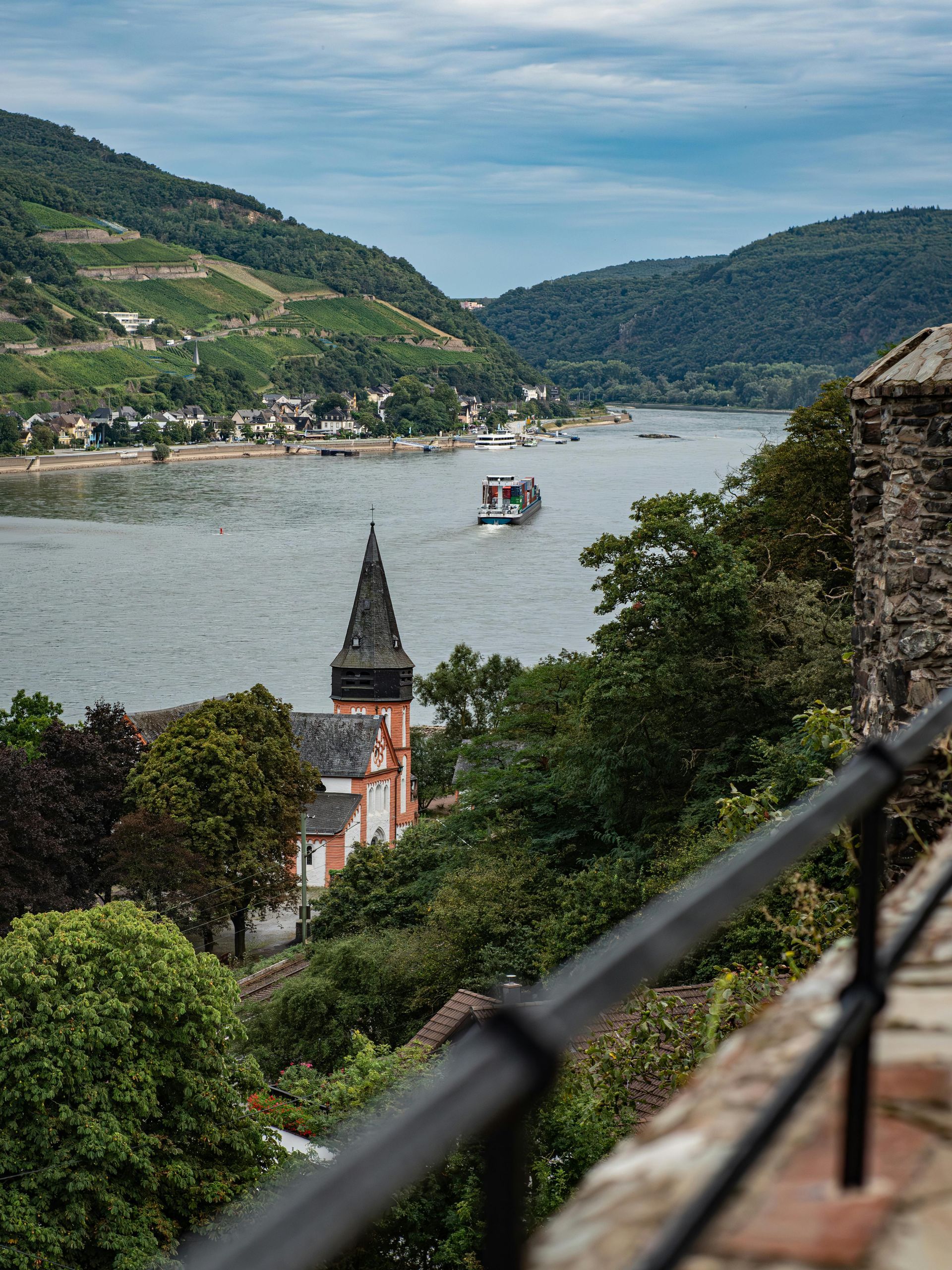 River cruise boat on Rhine River, church with tall spire, and hills with vineyards.
