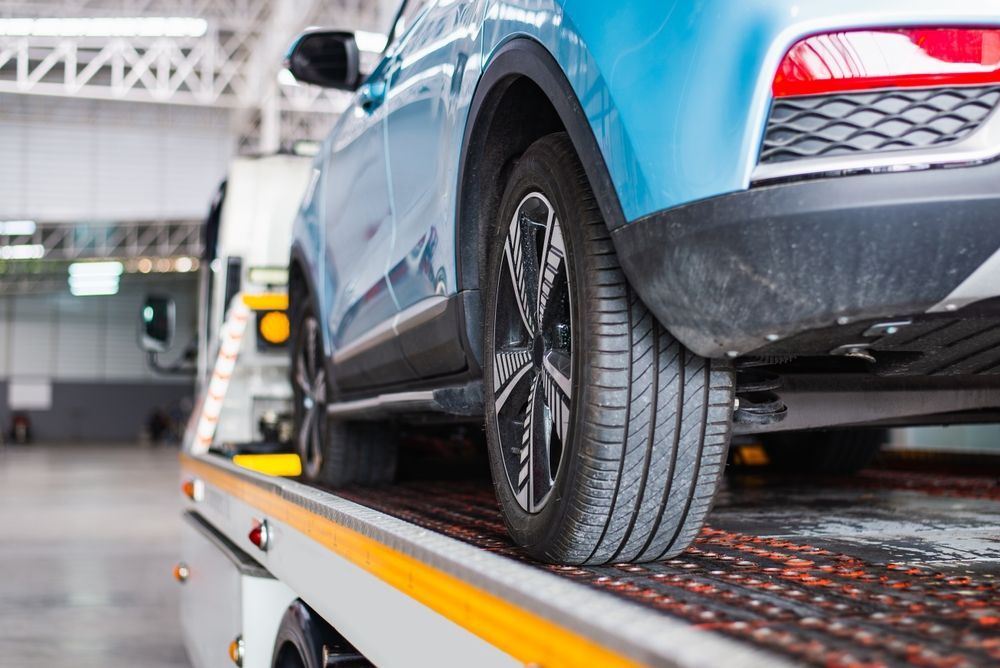 A blue car is sitting on top of a tow truck in a garage.