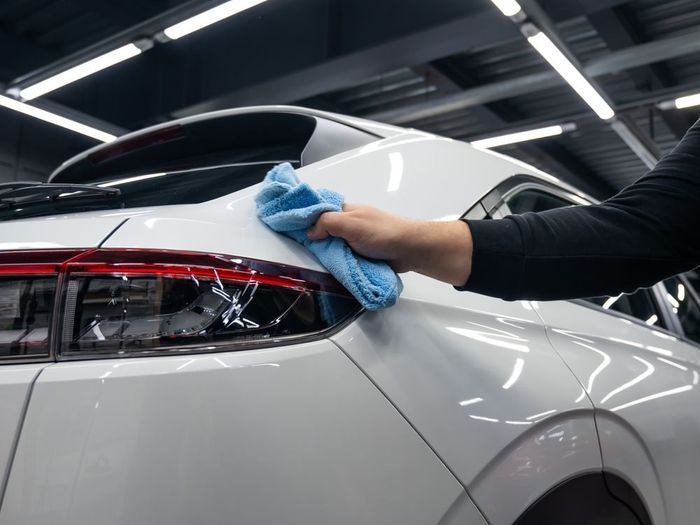 A person is cleaning a white car with a blue cloth.