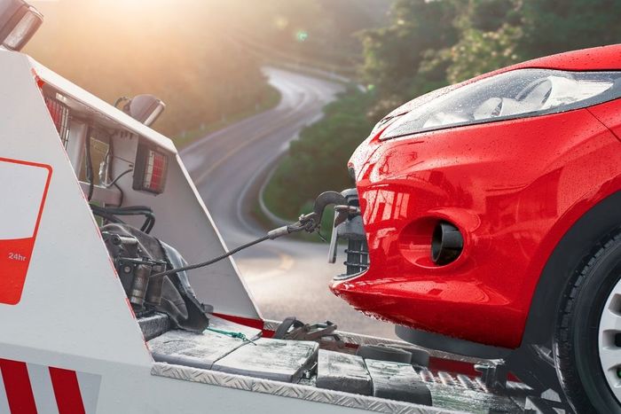 A red car is being towed by a tow truck.