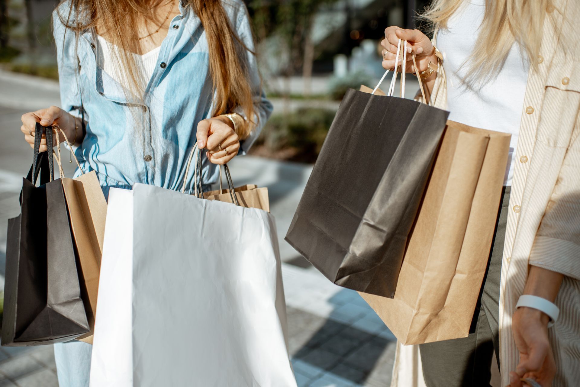 Two people hold several black, white, and brown paper shopping bags while standing outdoors.