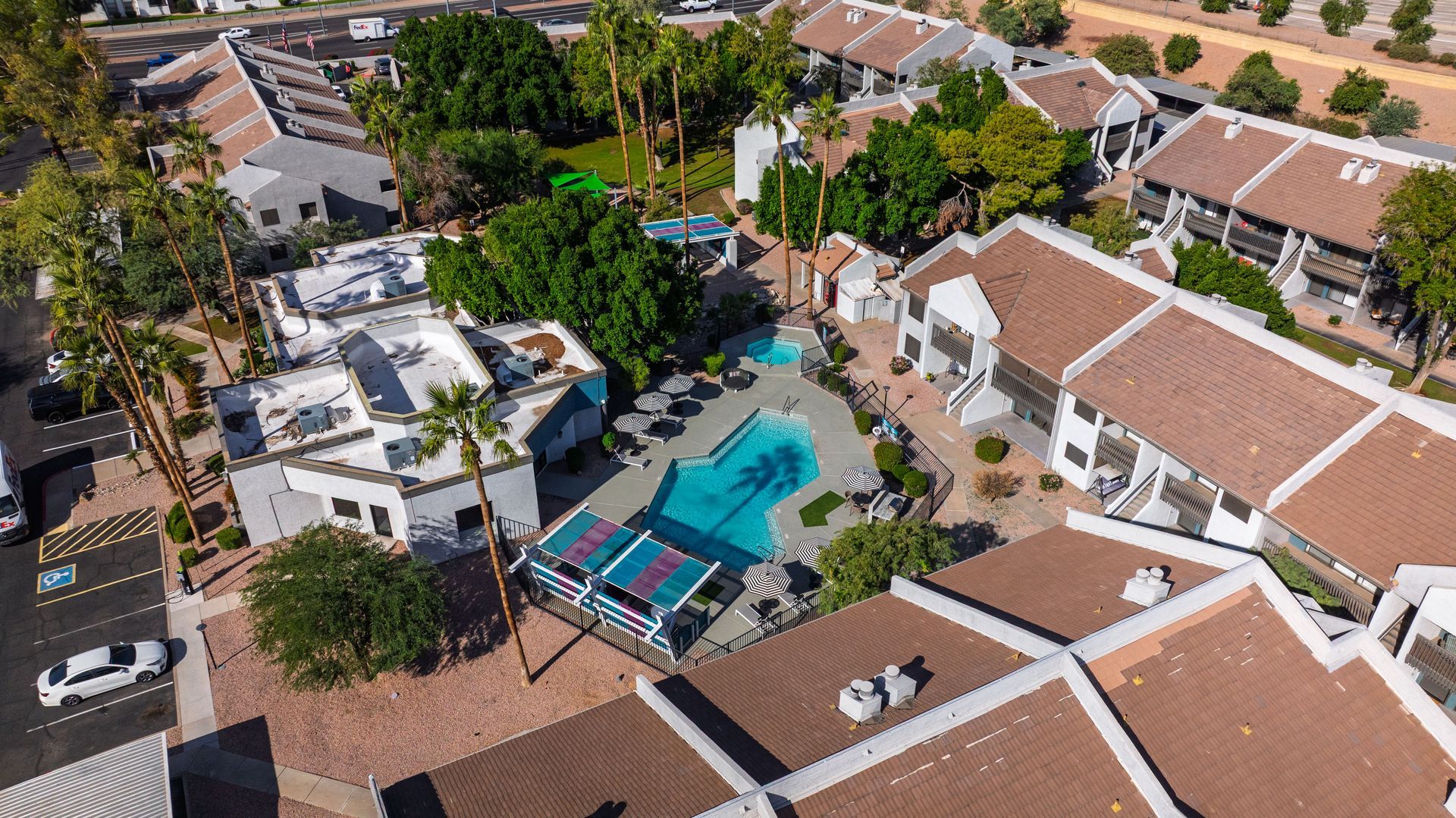 Aerial view of an apartment complex with a pool, parking, and brown tile roofs.