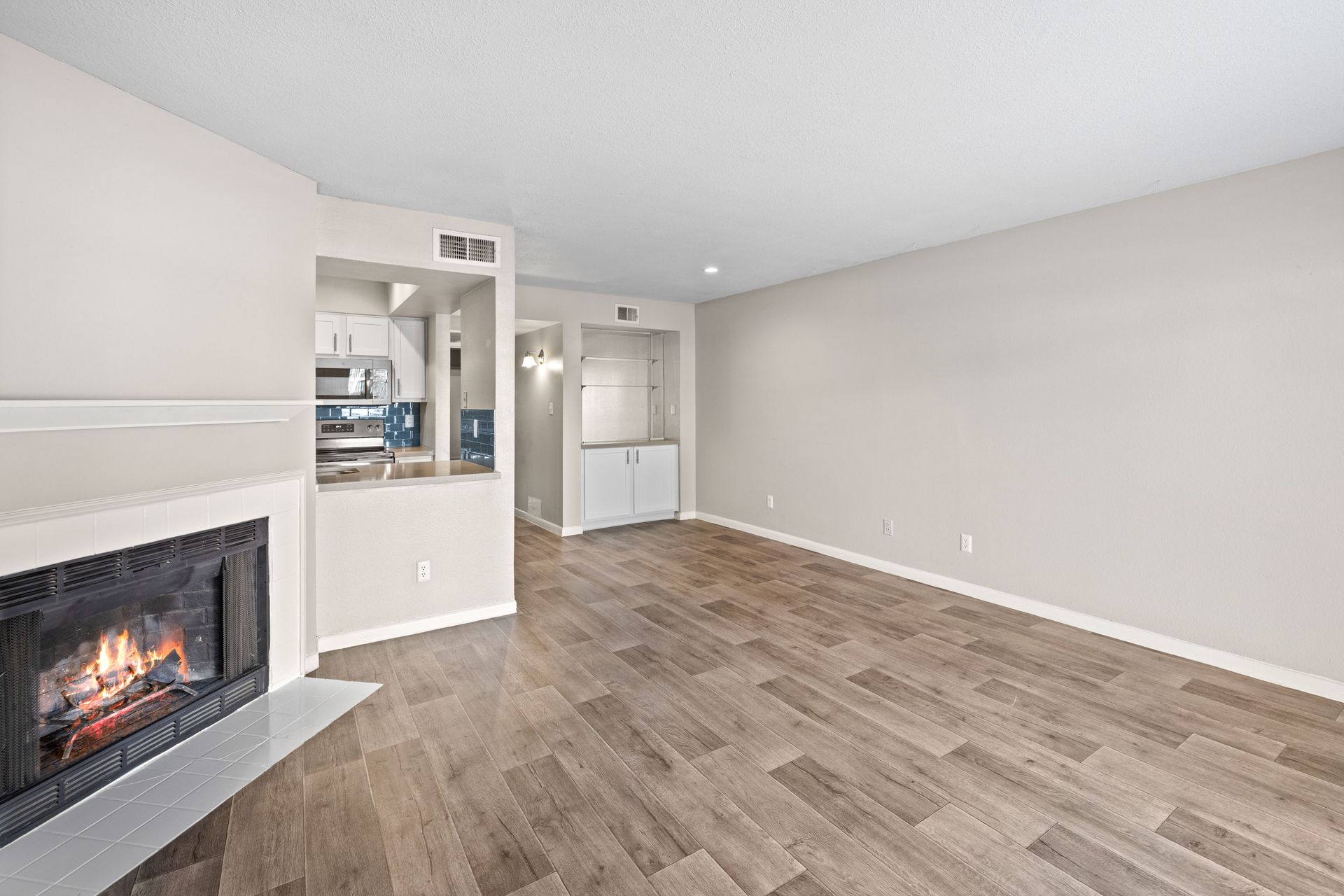 Empty apartment living room with fireplace and kitchen view. Light wood floors, neutral walls.