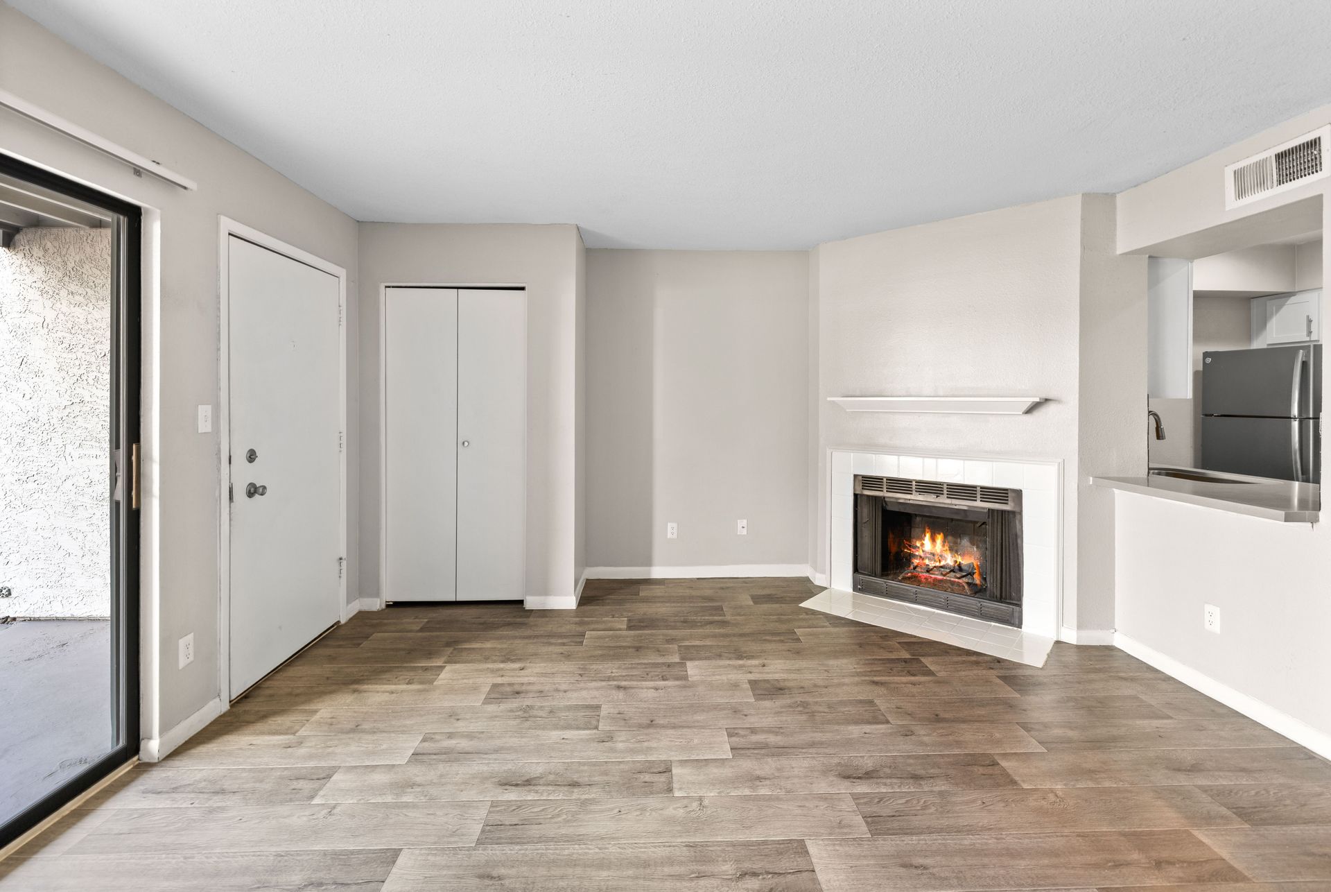 Empty living room with fireplace, sliding glass door, and faux wood flooring.