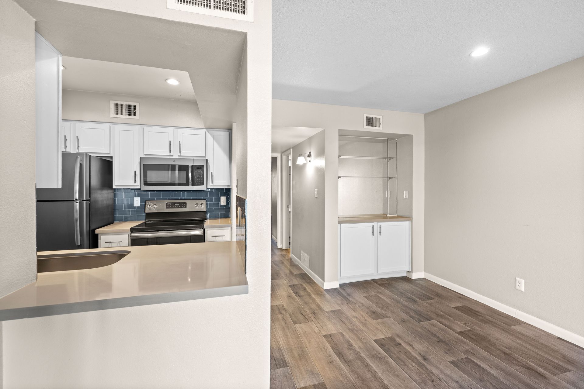 Interior view: Kitchen with white cabinets, stainless steel appliances, and adjacent living space with wood flooring.