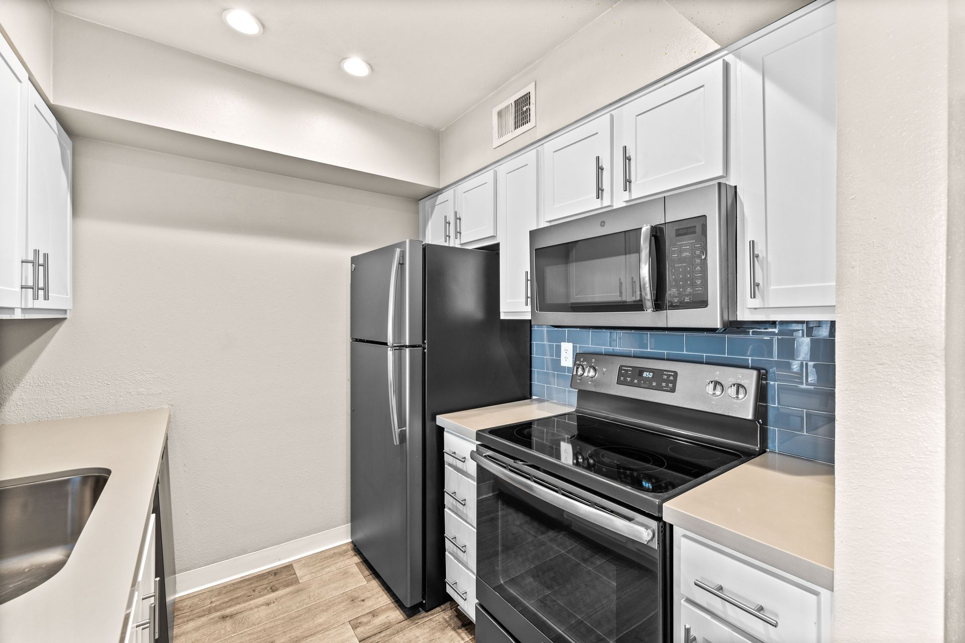 Small kitchen with white cabinets, stainless steel appliances, and blue tile backsplash.
