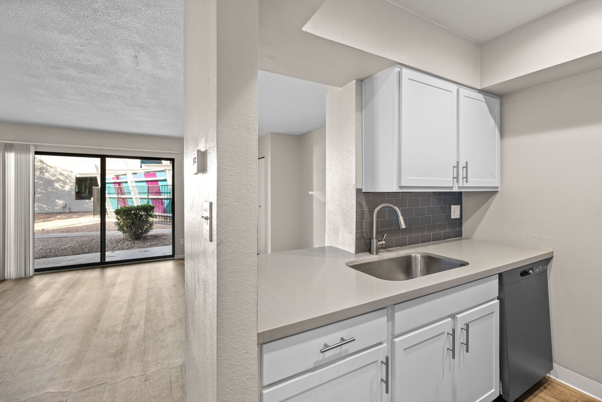 Kitchen with white cabinets, silver sink, and sliding glass door to exterior view.