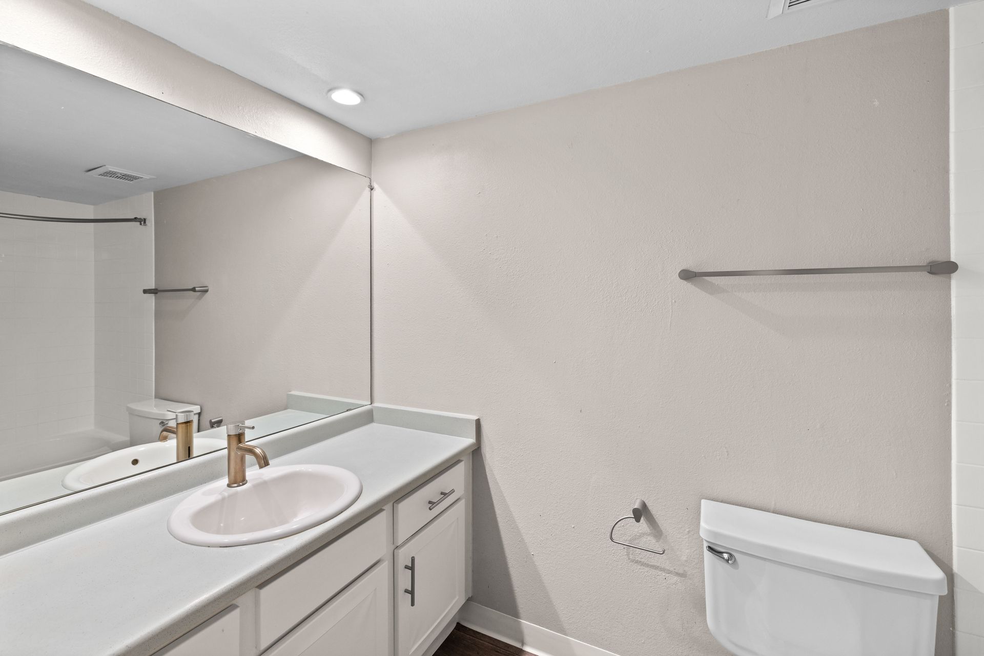 Bathroom with white vanity, sink, toilet, mirror, and towel rack on a light-colored wall.