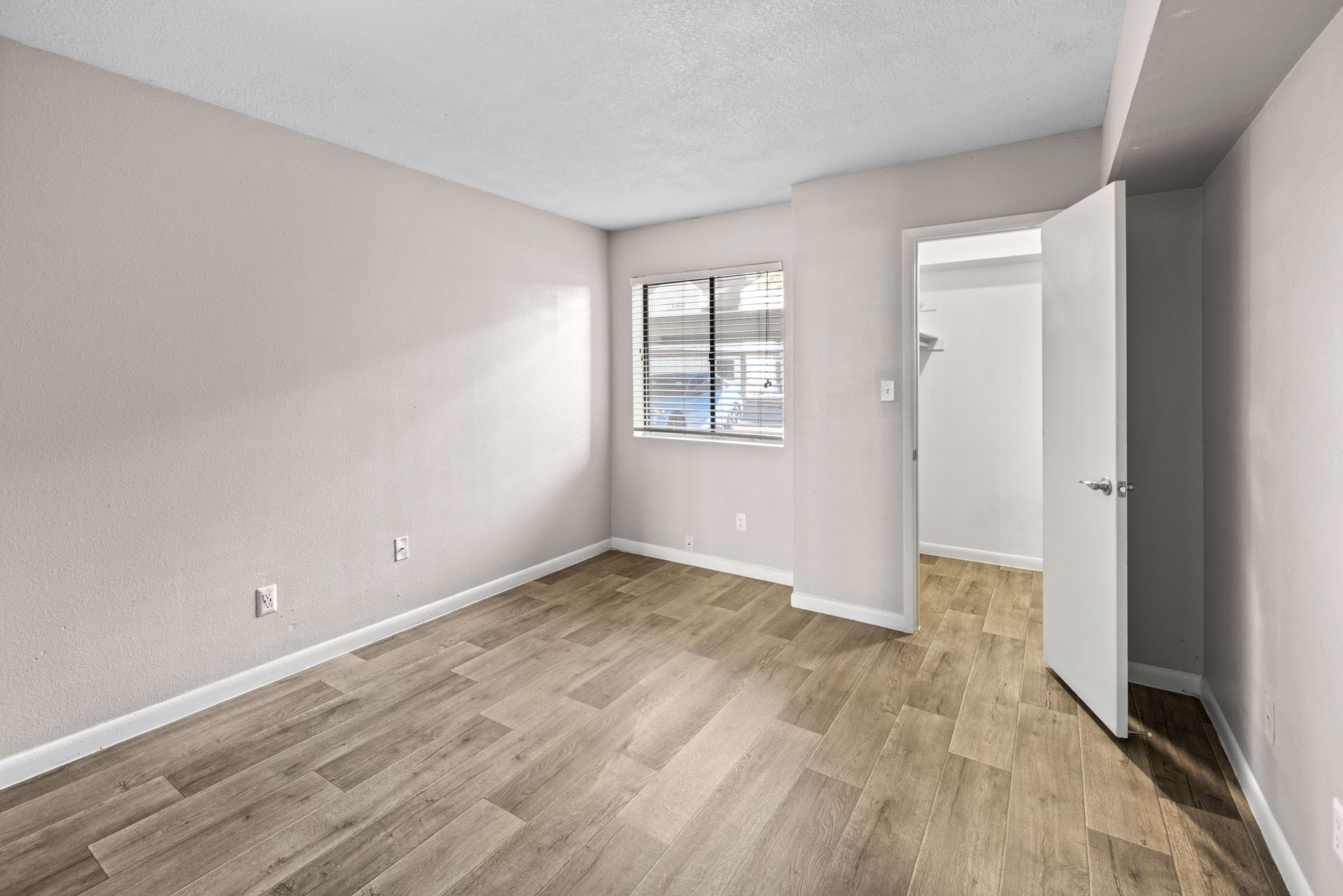 Empty bedroom with wood-look floor, window, closet, and pale gray walls.