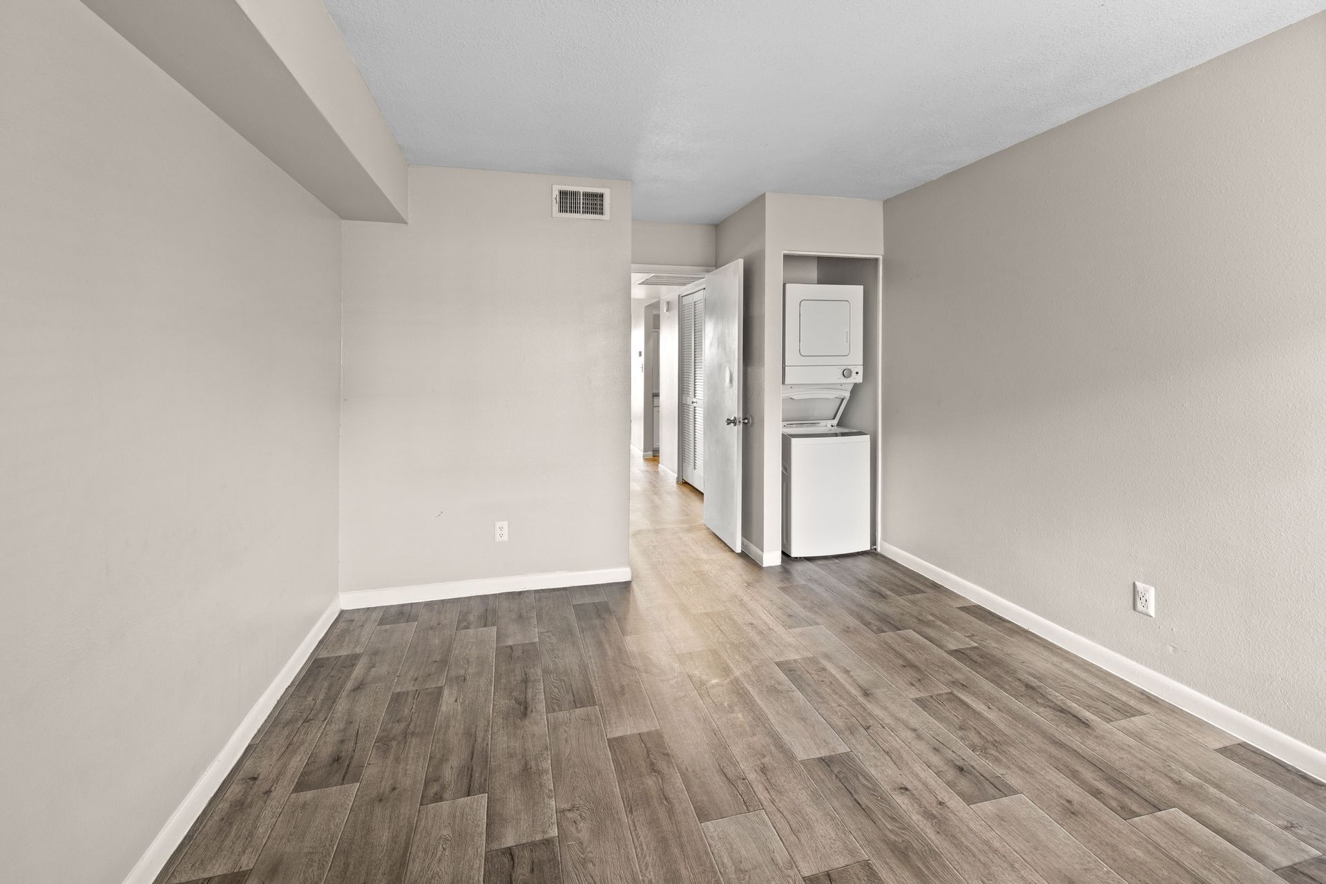 Empty room with wood-look flooring, light walls, and stacked washer/dryer.