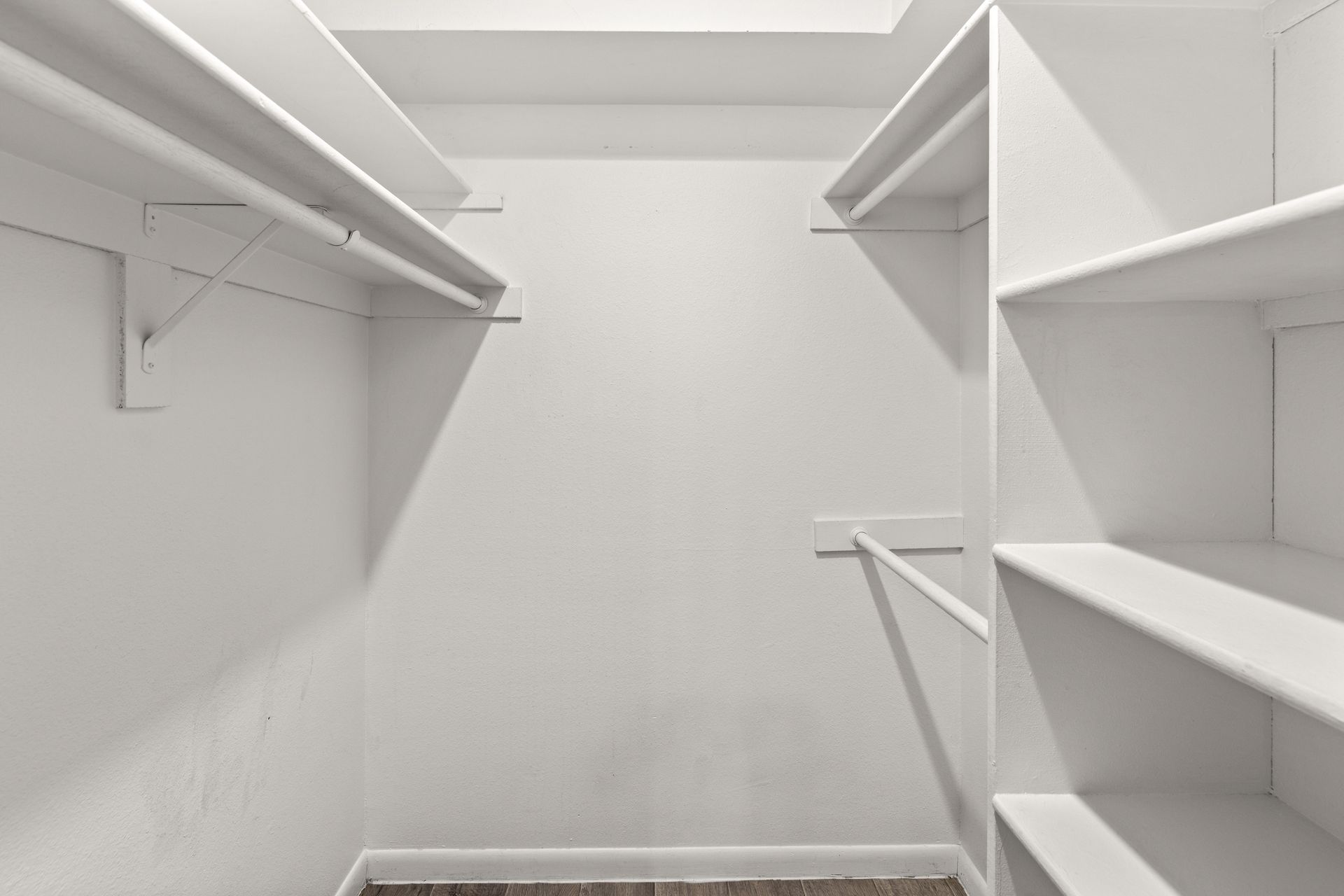Empty, white walk-in closet with shelves and hanging rods; a minimalist design for clothing storage.
