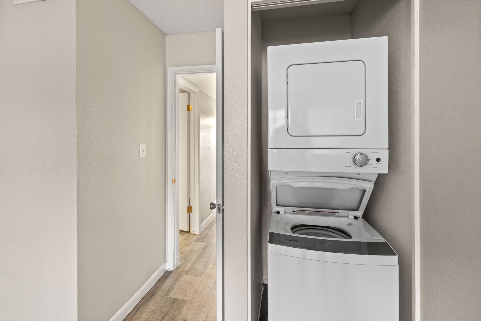 Stacked white washer and dryer in a small closet; hallway visible.