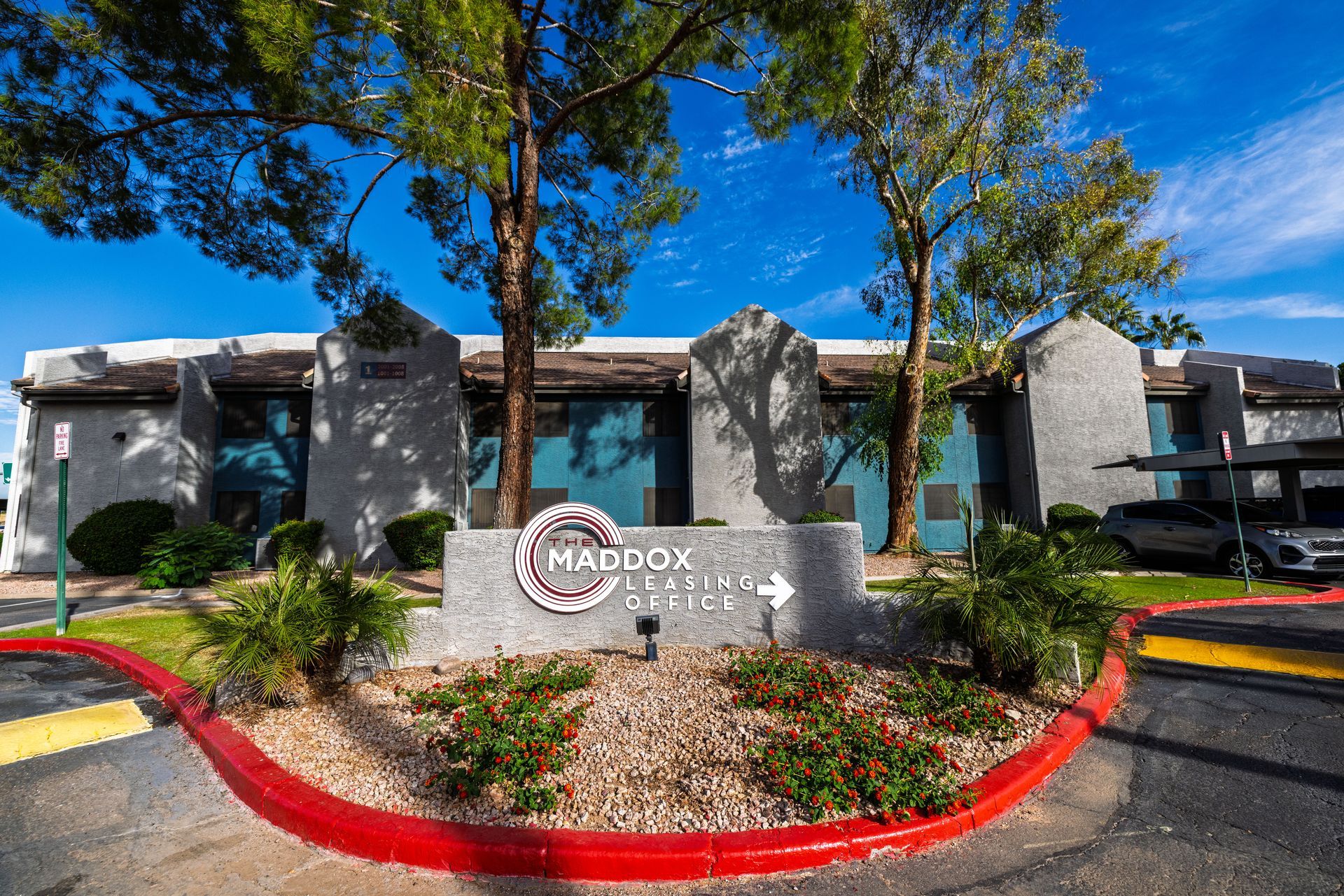Sign for Maddox Apartments with an arrow, flanked by trees and bushes. Building in the background at the Maddox.