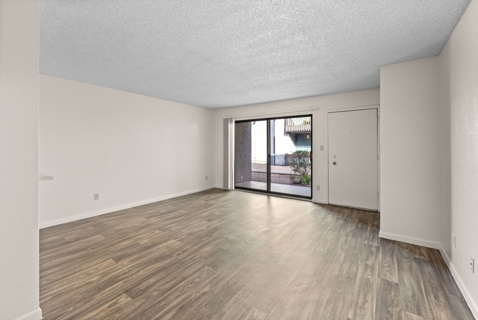 Empty room with wood-look floor, sliding glass door to outside, and white walls and ceiling.