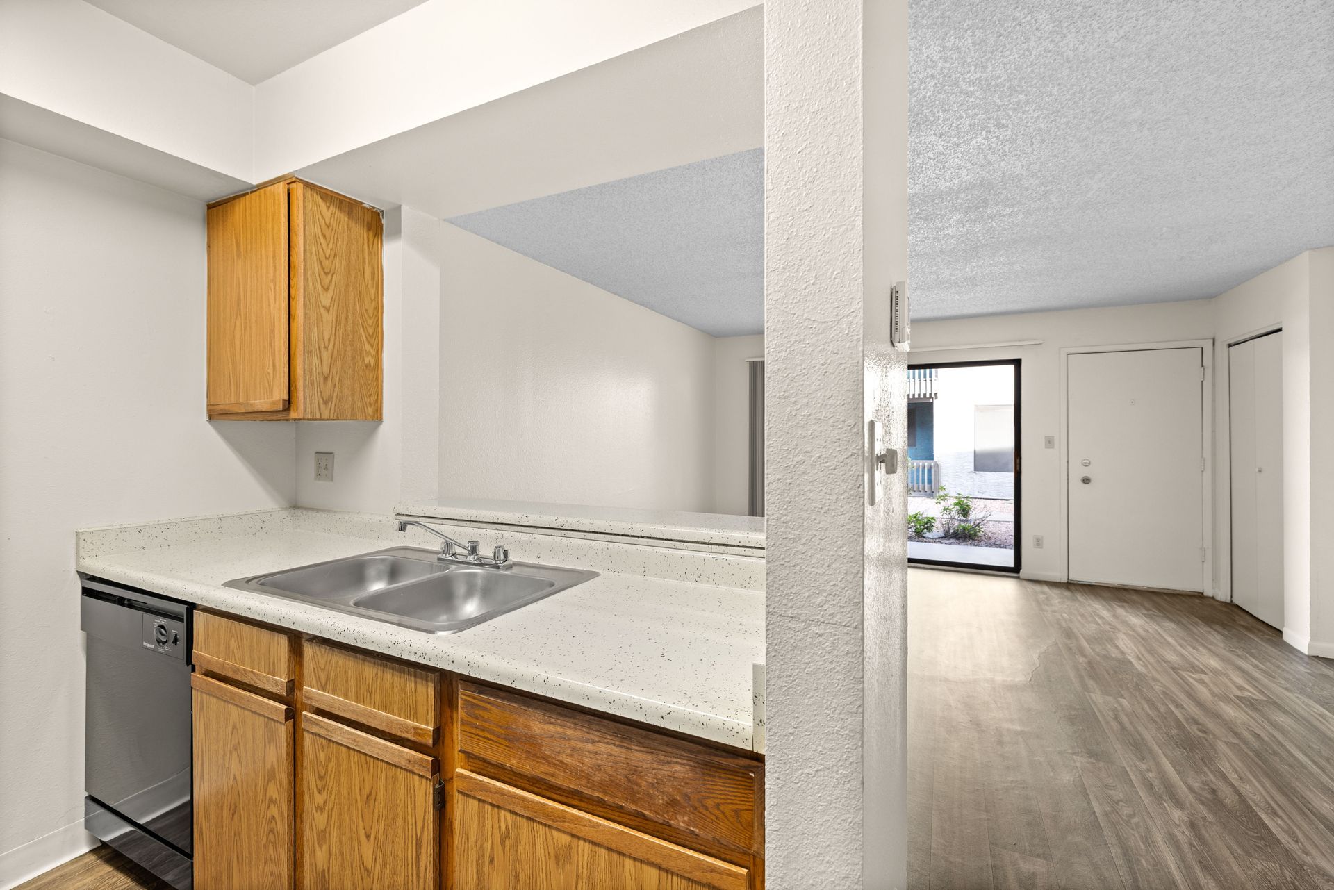 Kitchen with wooden cabinets, light countertops, and stainless steel sink, with view to a living space.