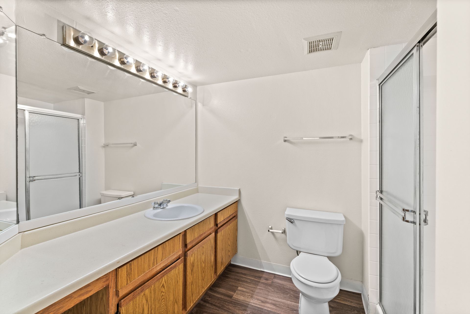 Bathroom with white countertop, brown cabinets, toilet, and glass shower.