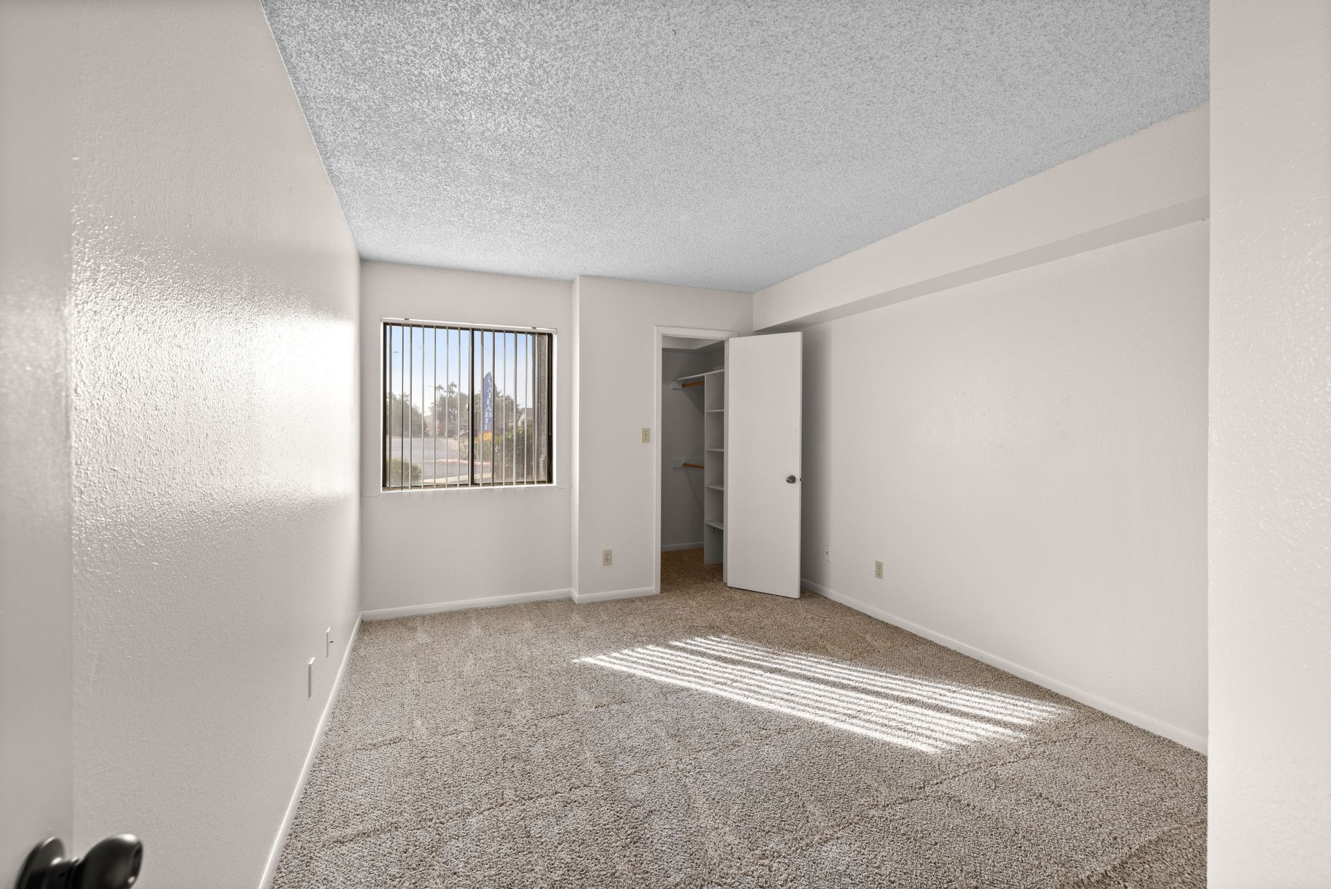 Empty bedroom with beige carpet, white walls, and a window with blinds.