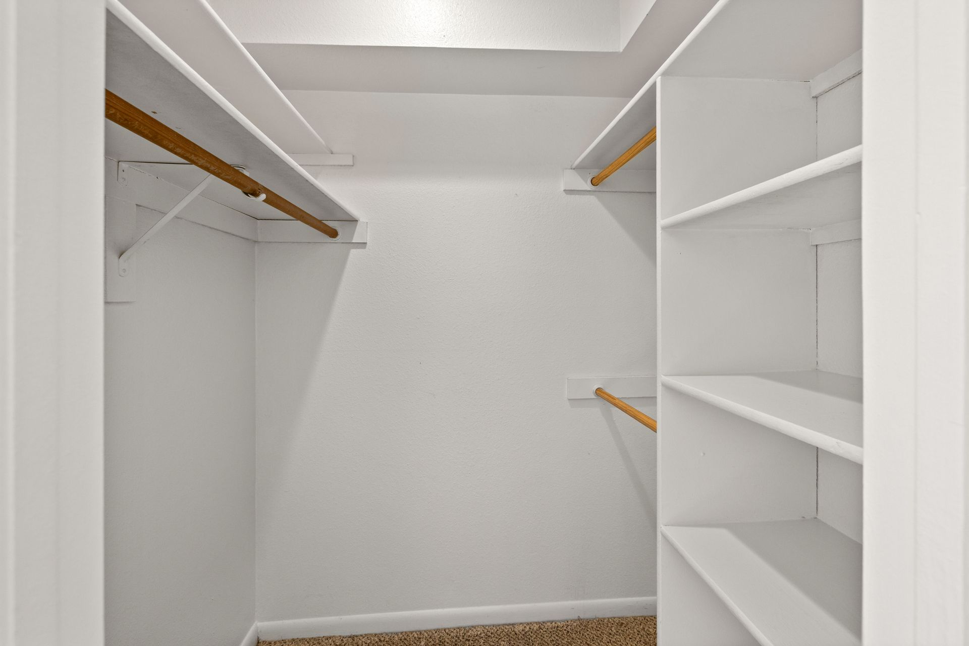 Empty white walk-in closet with shelves and rods, neutral color scheme.