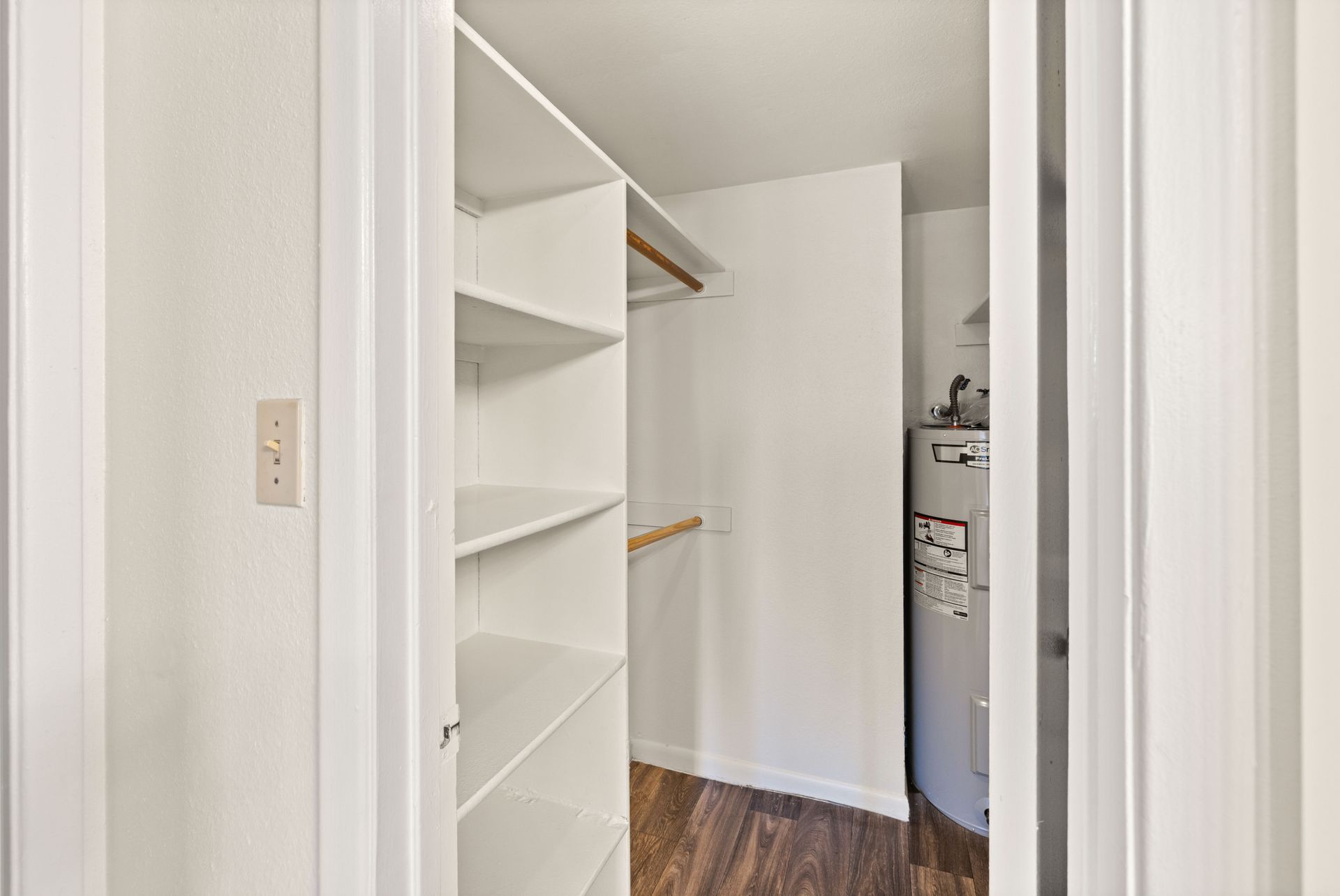 Empty white closet with shelves and clothes rod; wooden floors, neutral walls.