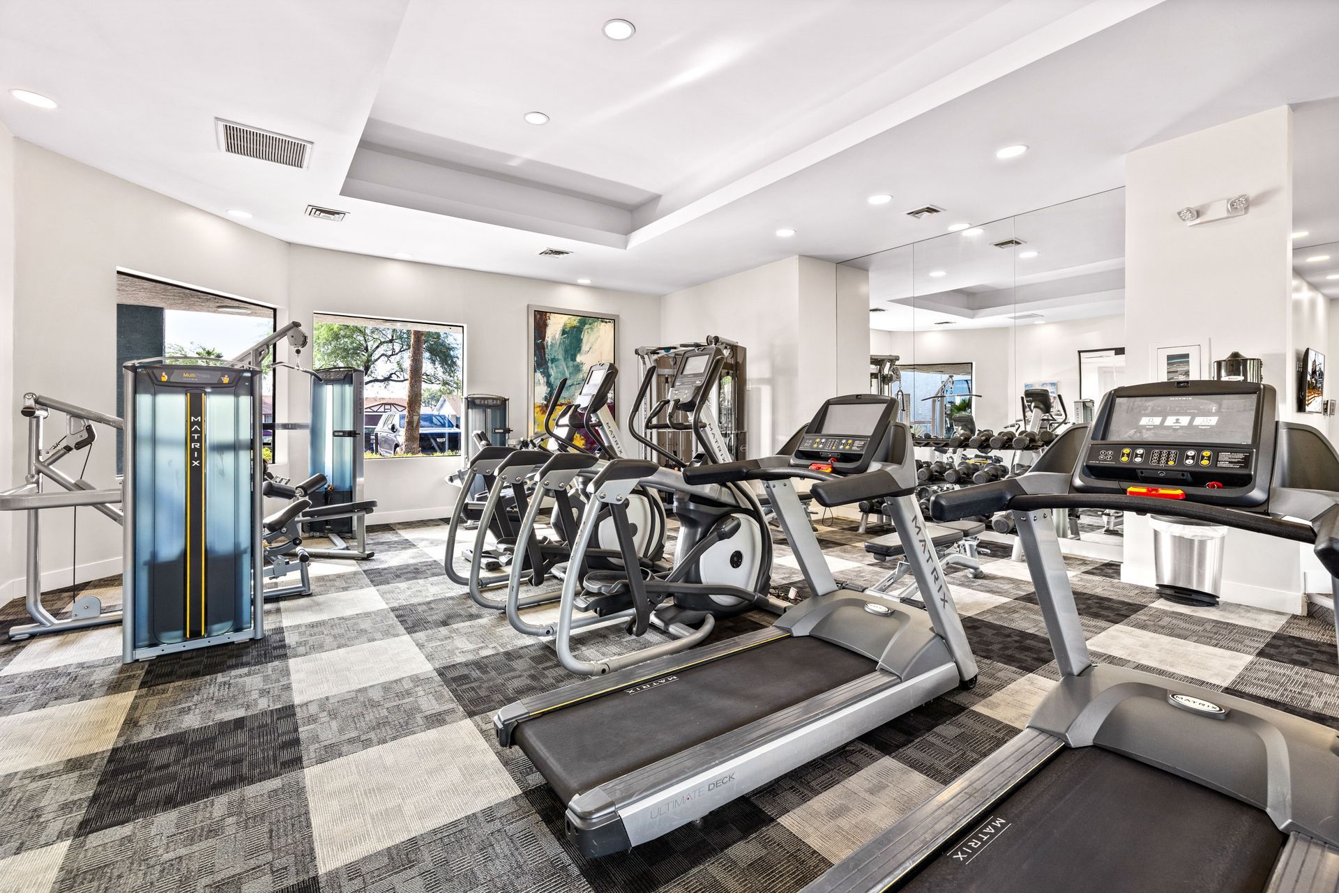 Gym interior with exercise machines, mirrors, and checkered flooring.