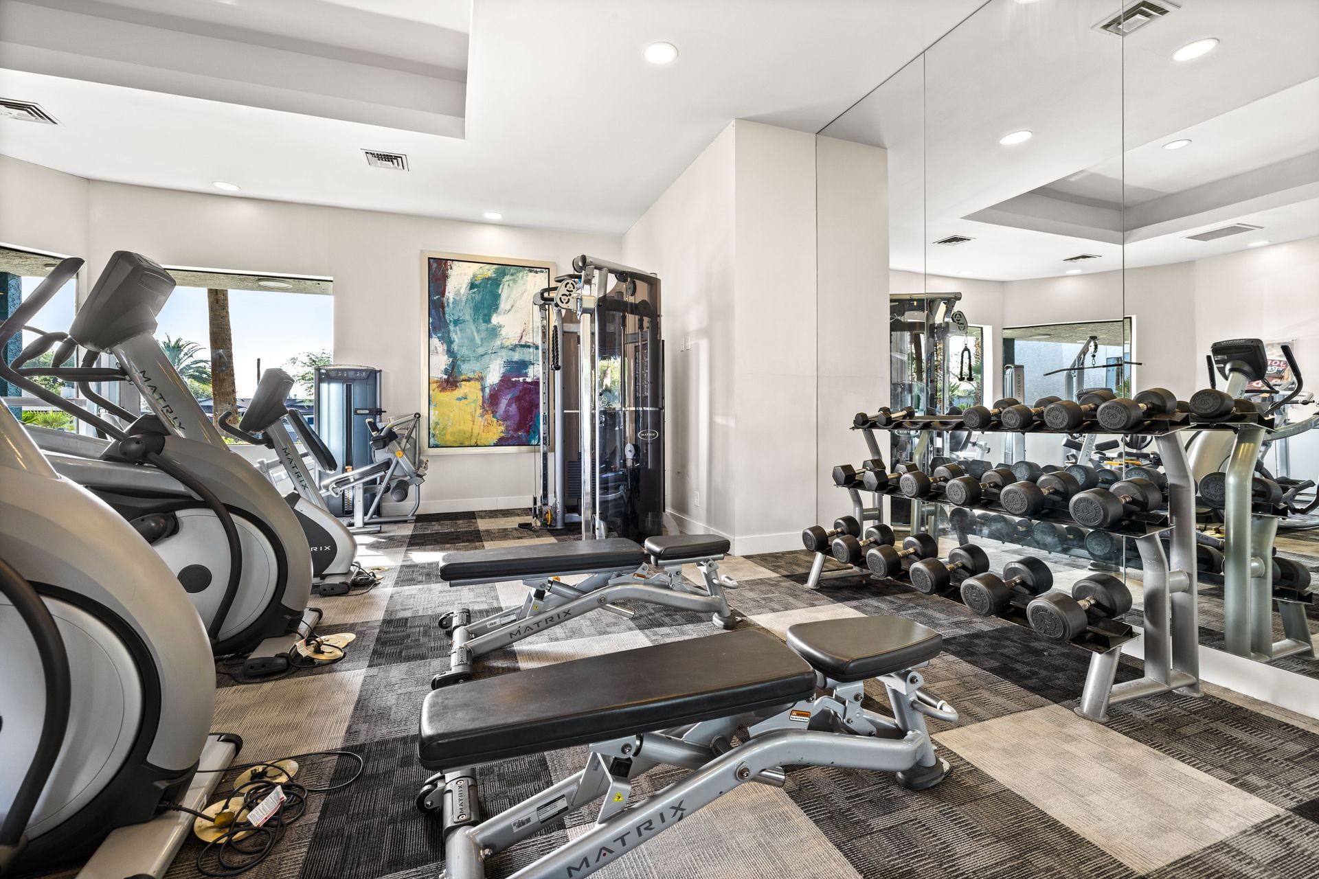 Gym interior with exercise equipment, dumbbells, and mirrors.