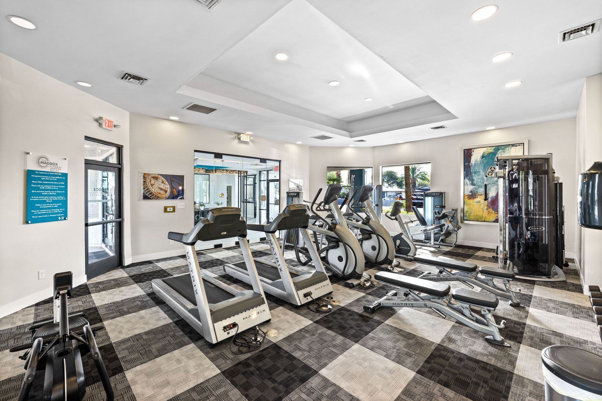 Gym with treadmills, elliptical machines, weight bench, and exercise equipment on a patterned floor.