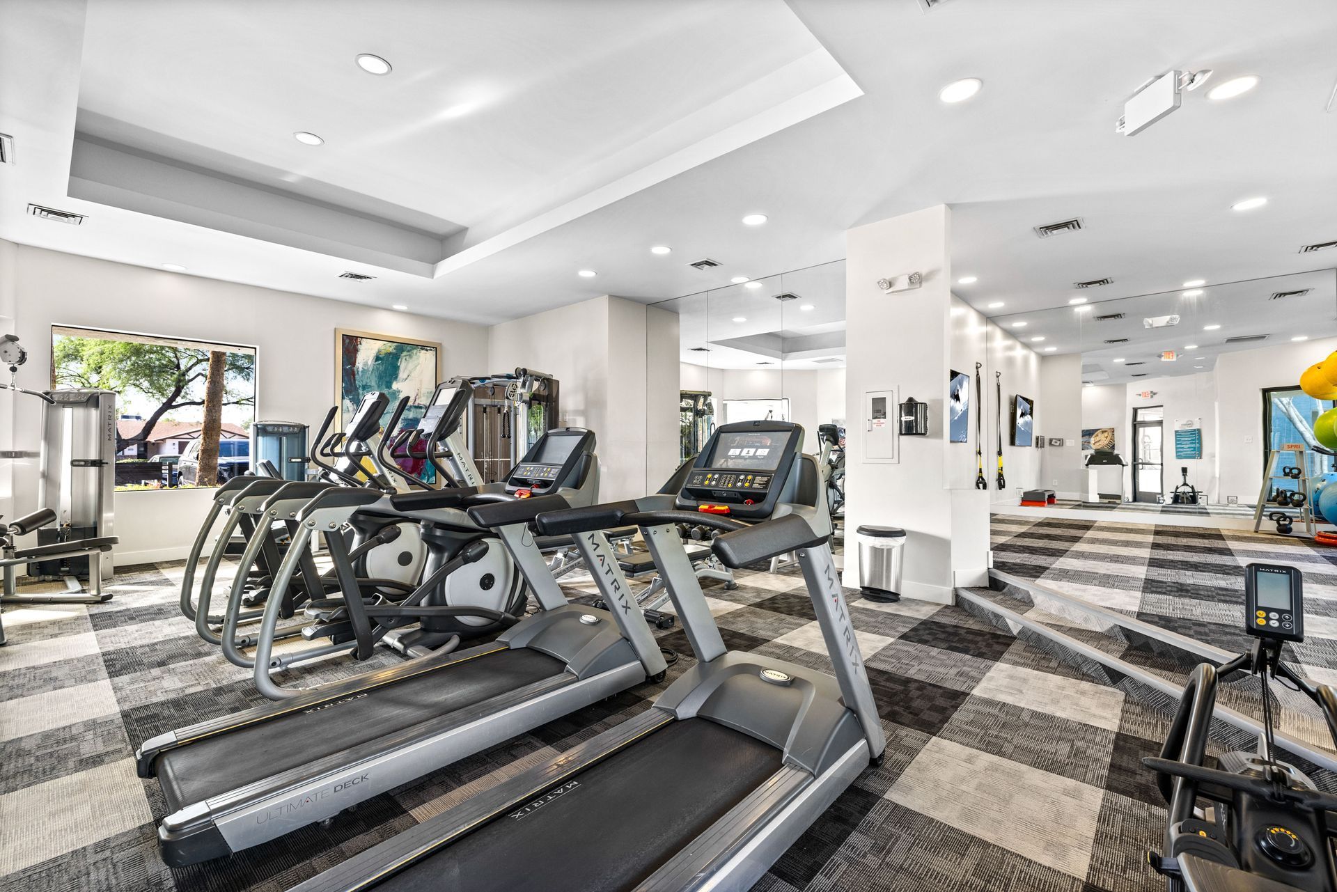 Gym interior with treadmills, exercise bikes, and other equipment on a patterned floor.