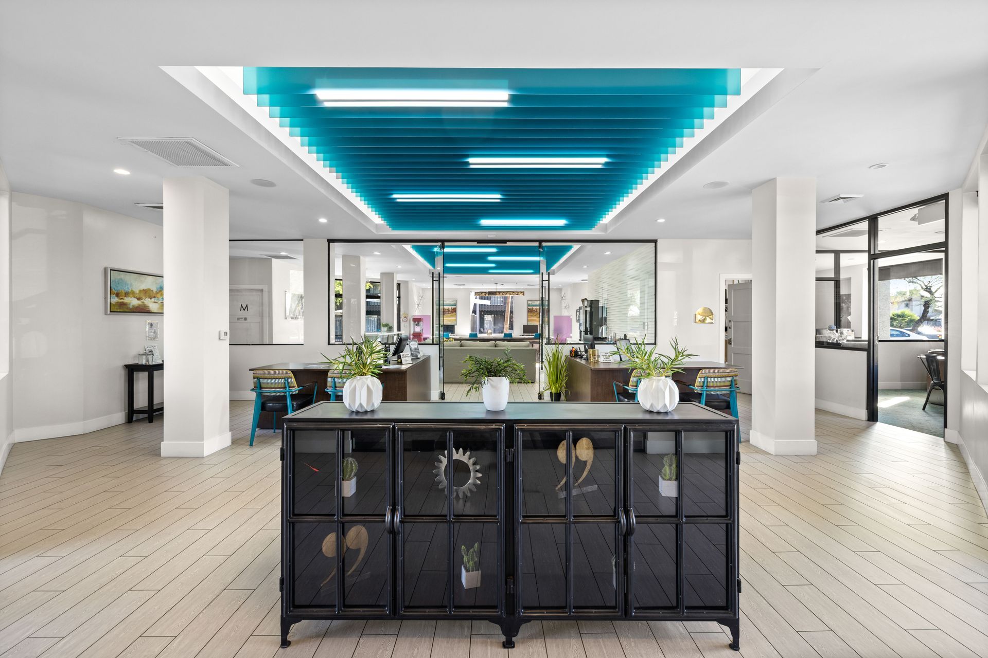 Reception area with black cabinet, turquoise ceiling lights, and open views to workspace.