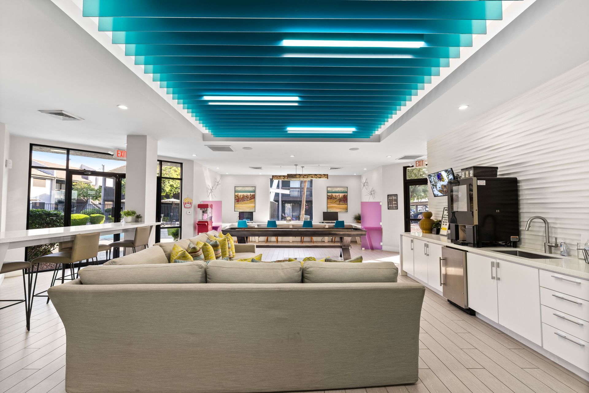 Lounge area with a gray couch, white cabinets, and a blue, geometric ceiling.