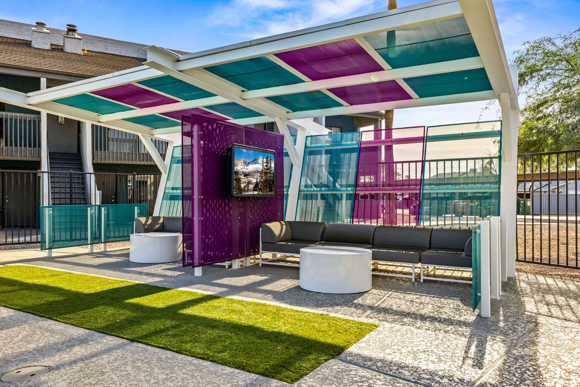 Outdoor lounge area with colorful canopy and seating. Purple, teal, and white structure with a TV.