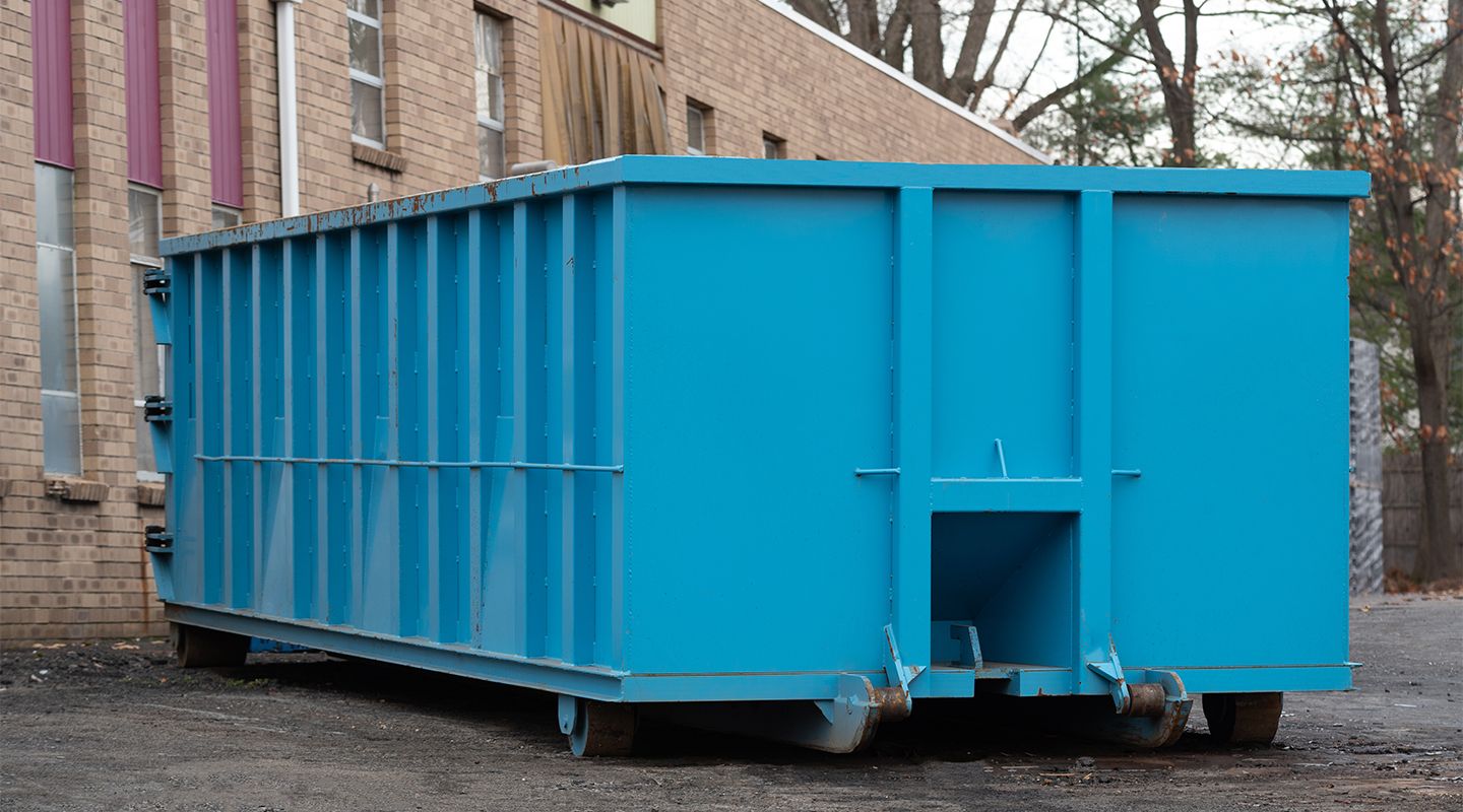 Large bright blue industrial dumpster on wheels beside a brick building outdoors