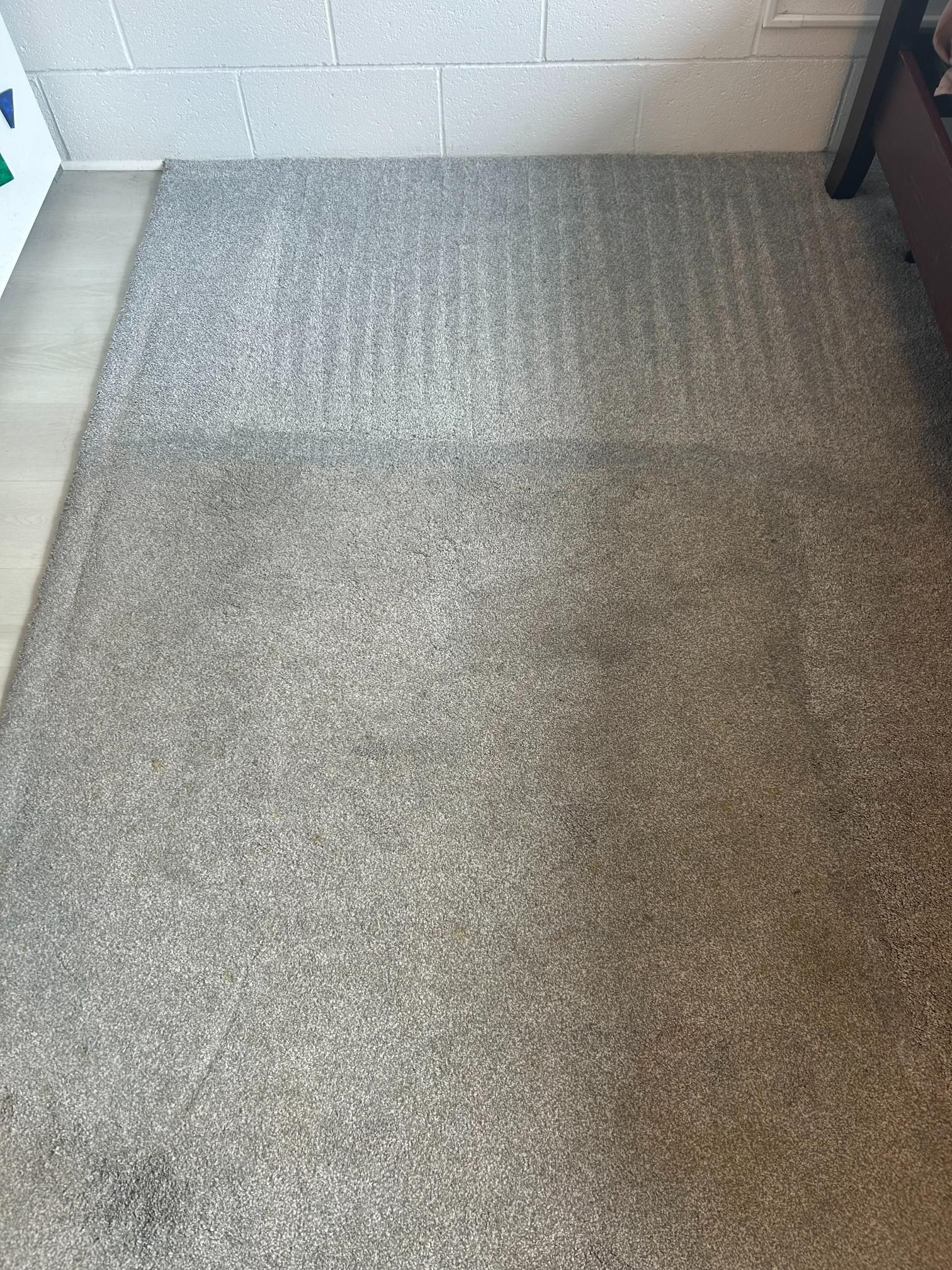 A gray carpet is sitting on a tiled floor next to a white wall.