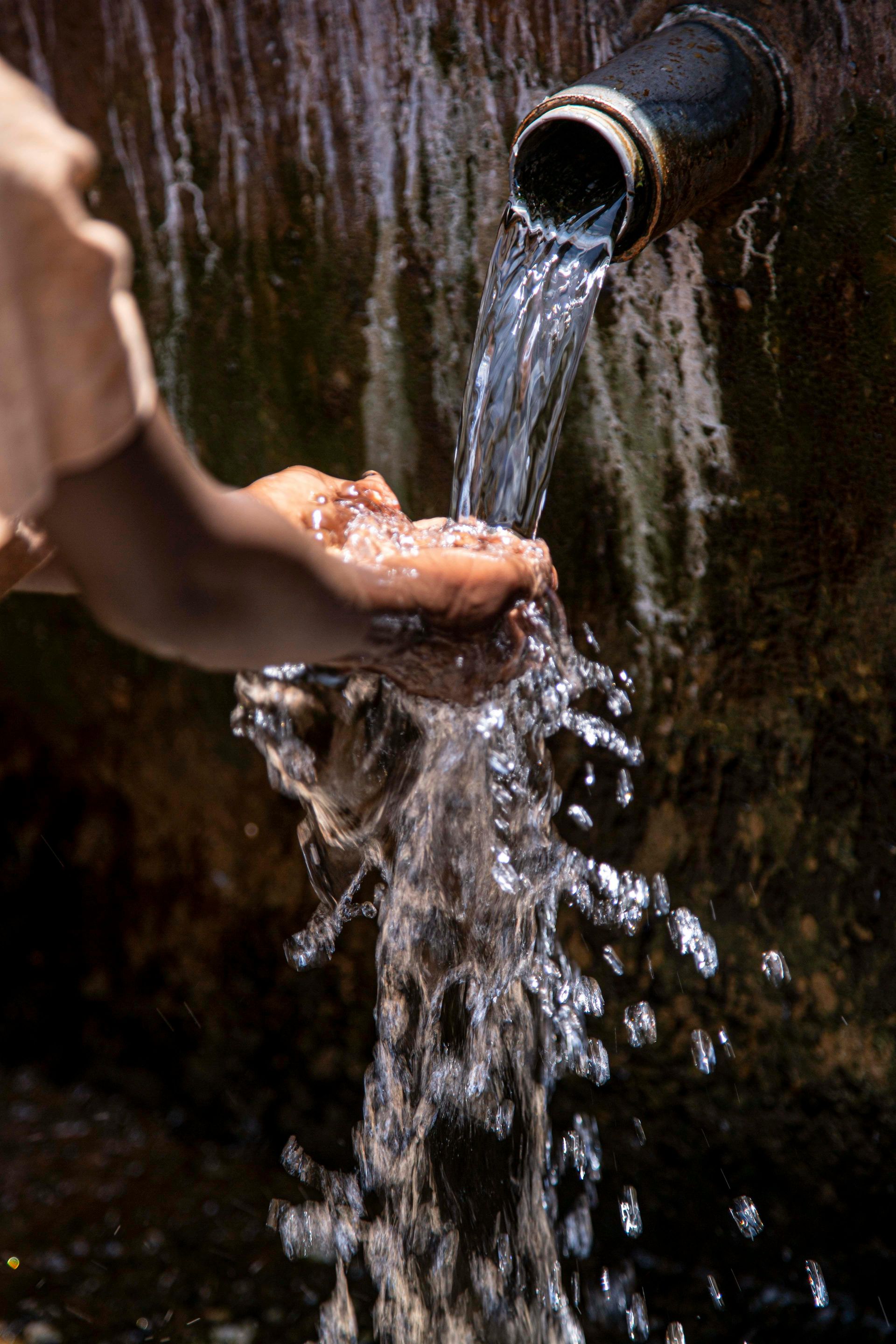 A person is washing their hands with water from a pipe.