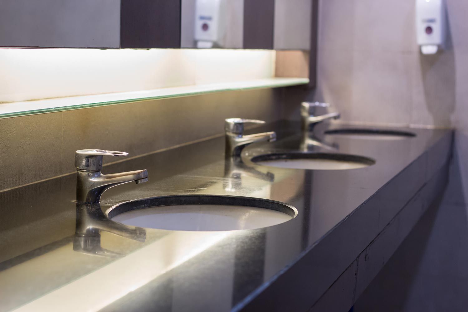 Row of modern stainless steel bathroom sinks with chrome faucets on a countertop