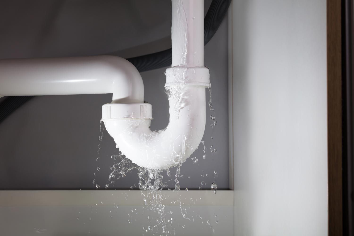 Leaking white drain pipe under a sink, water dripping into a cabinet.