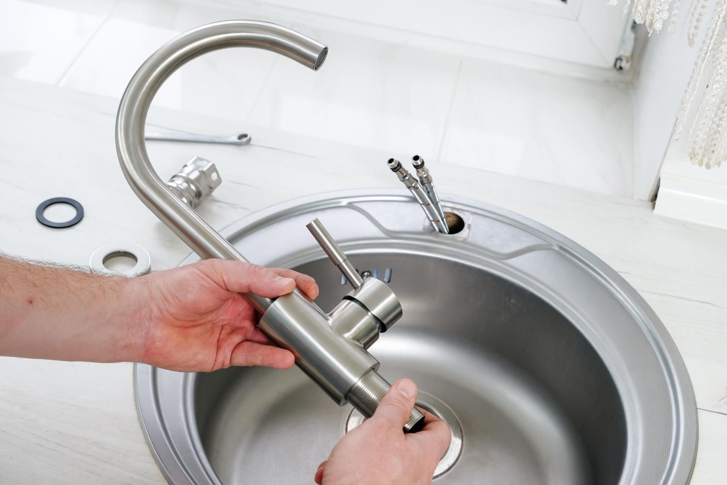 A pair of hands holds a stainless steel kitchen faucet over a stainless steel sink during installation.
