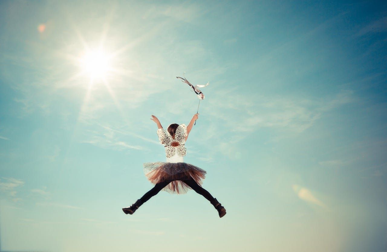 Person jumping joyfully in midair against a bright blue sky, sun shining nearby