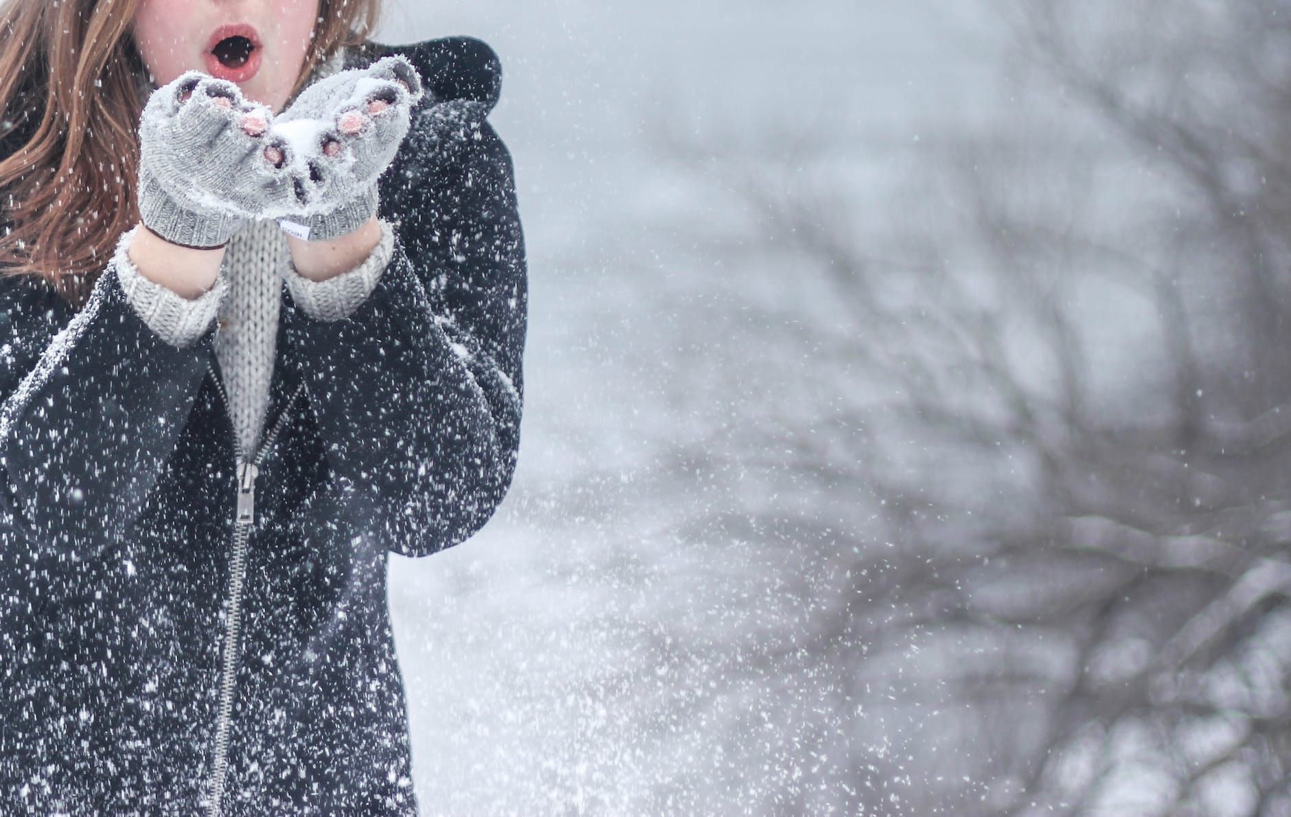 Person in a dark coat catching falling snow in gloved hands outdoors