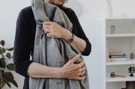 A person in a black long-sleeved shirt holds a folded gray wool coat against their chest in a bright, modern room. A person in a black long-sleeved shirt holds a folded gray wool coat against their chest in a bright, modern room.