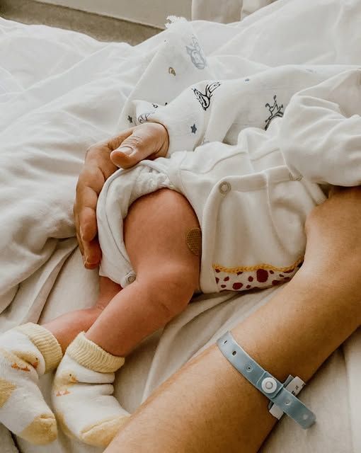 Close-up of a sleeping baby cuddled in white blankets, with an adult hand gently holding them.