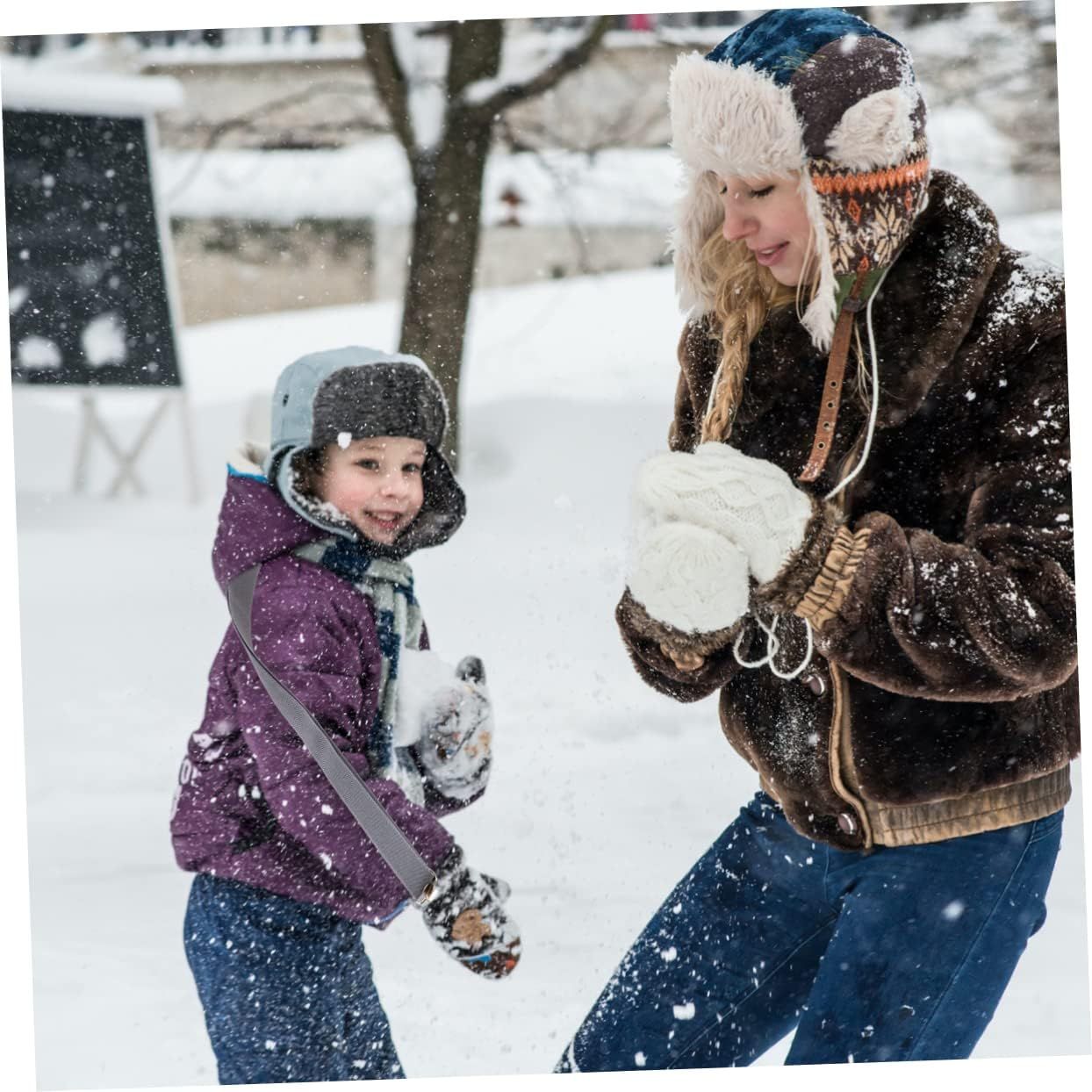 Two people in winter clothes having a snowball fight outdoors in falling snow