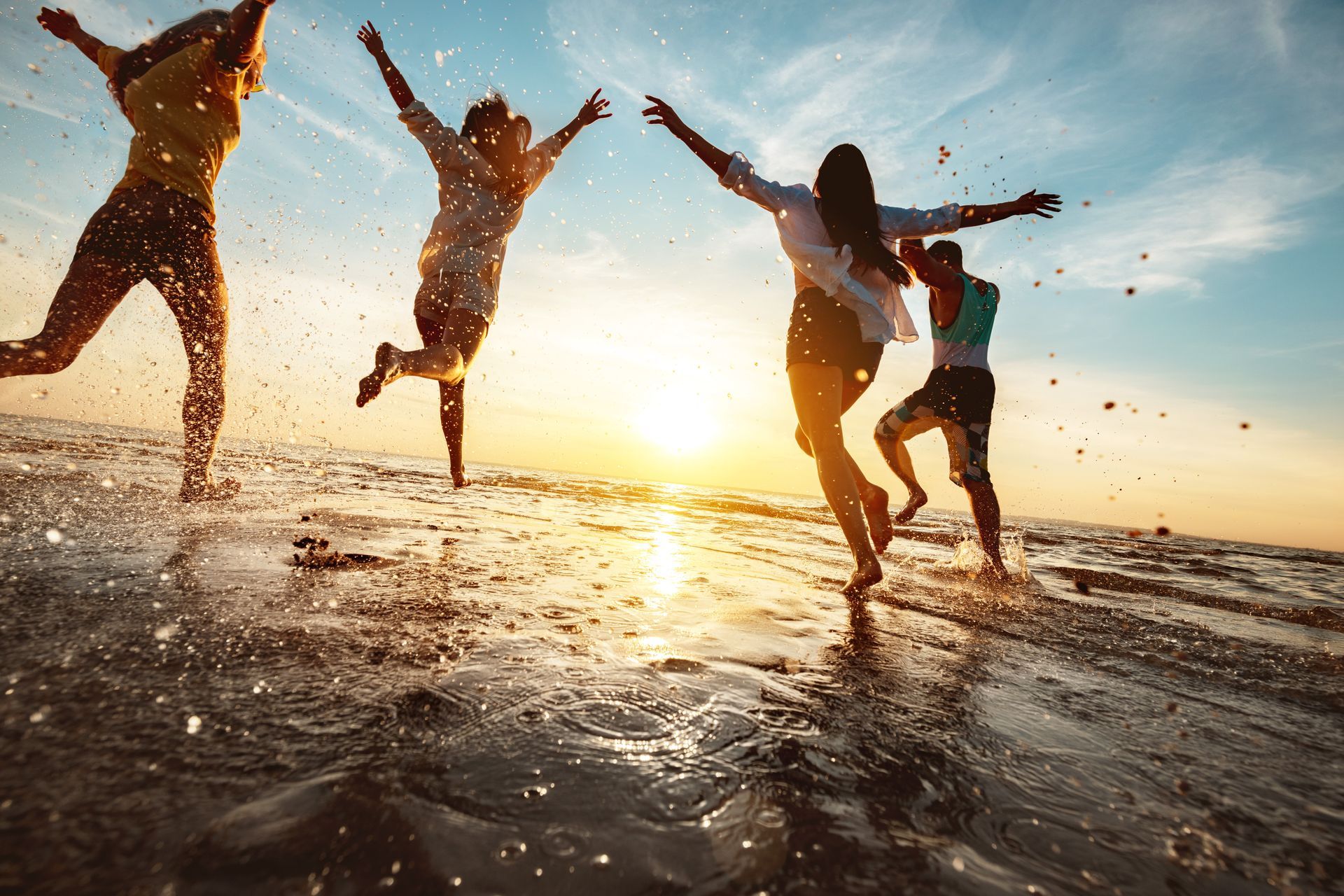 People jumping and splashing in the ocean at sunset on a beach