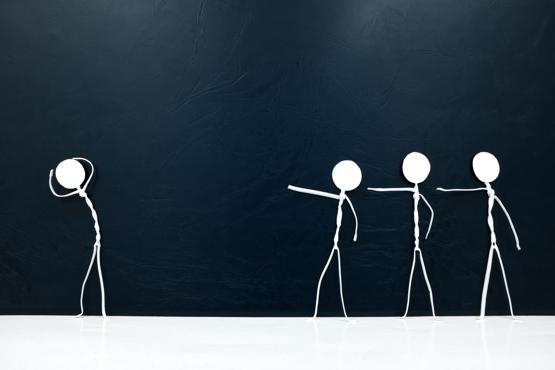 A stick figure stands alone, head in hands, while three other stick figures point and gesture toward them.