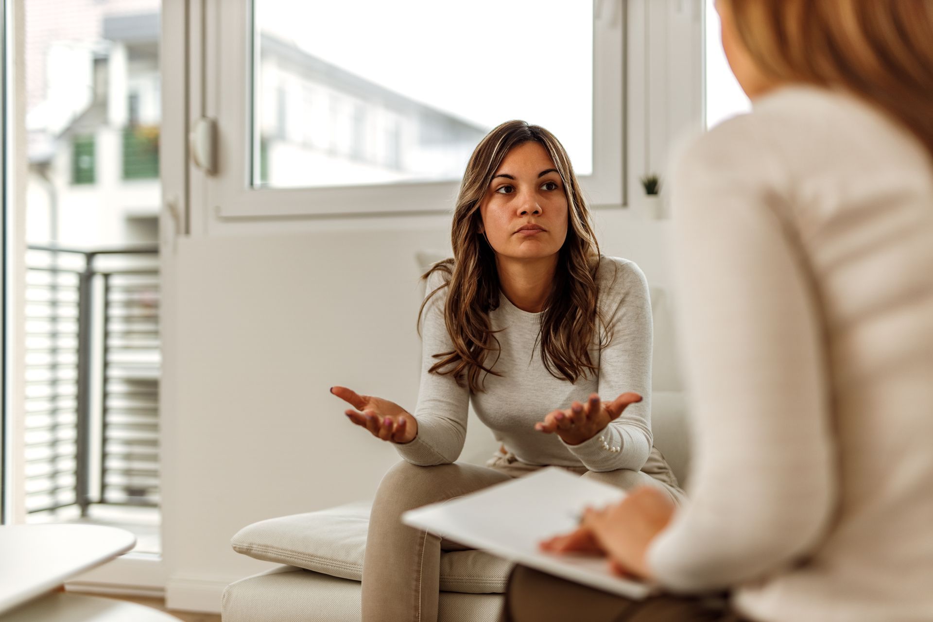 Two people in a bright office during a conversation, one speaking with hands raised while the other