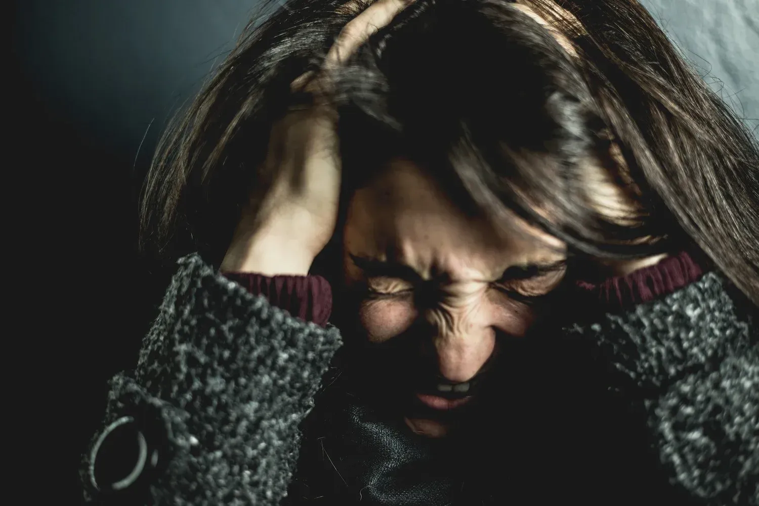 A person holding their head with both hands, eyes tightly closed and face contorted in an expression of distress. A person holding their head with both hands, eyes tightly closed and face contorted in an expression of distress.