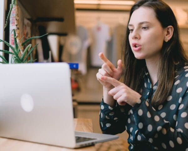 Woman gesturing while talking on a video call beside a laptop in a cozy indoor setting