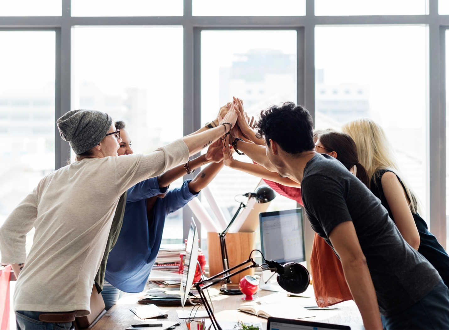 Coworkers giving a group high-five around desks in a bright office